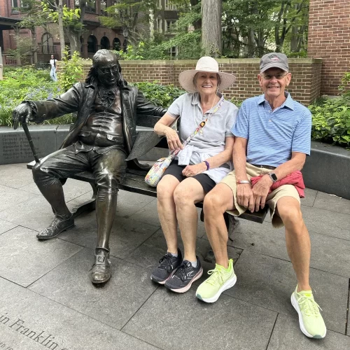 A Penn donor couple seated beside the Benjamin Franklin statue on Penn's campus