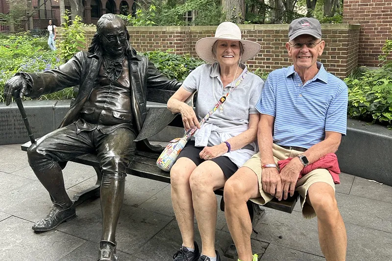 A Penn donor couple seated beside the Benjamin Franklin statue on the University’s campus