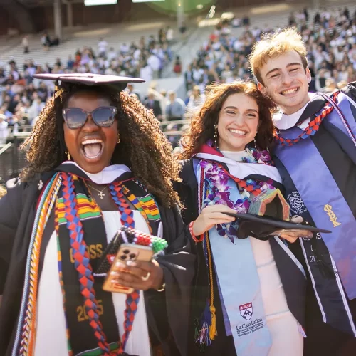 Three students in graduation regalia show their exuberation during Commencement at Penn.
