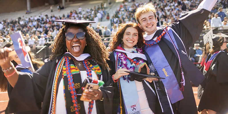 Three students in graduation regalia show their exuberance during Commencement at Penn.