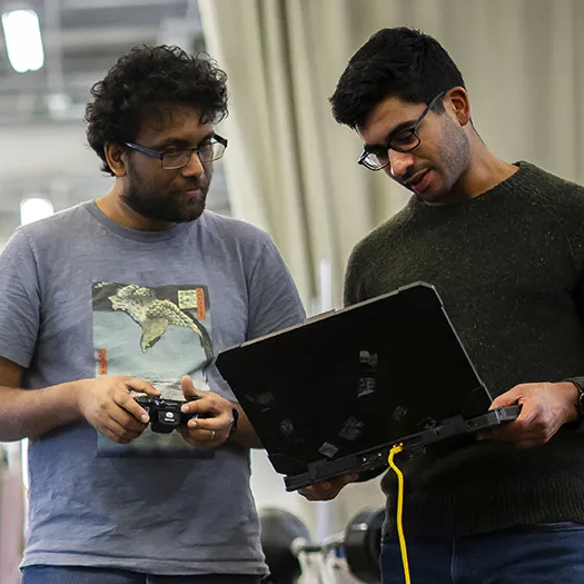 Two students monitor readings on a laptop as they conduct an engineering experiment together.
