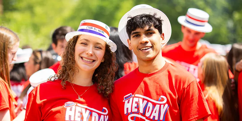 Two smiling Penn students wearing red Hey Day shirts and white hats pose for a photo during the 2025 celebration.