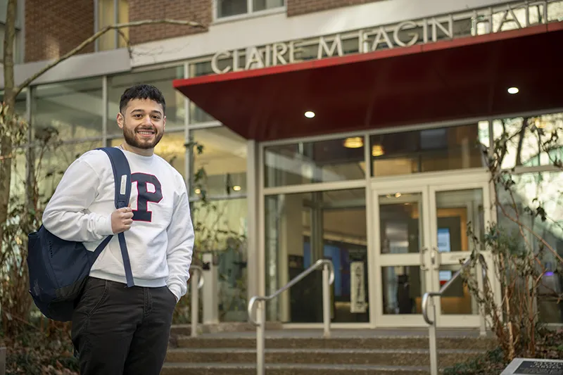 Penn student in a white sweatshirt stands confidently in front of Fagin Hall.