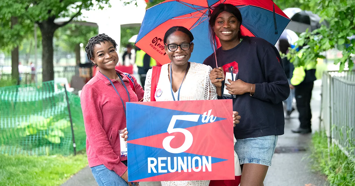 Alumni gather in the rain to celebrate their 5th Penn reunion with bright umbrellas and happy expressions.