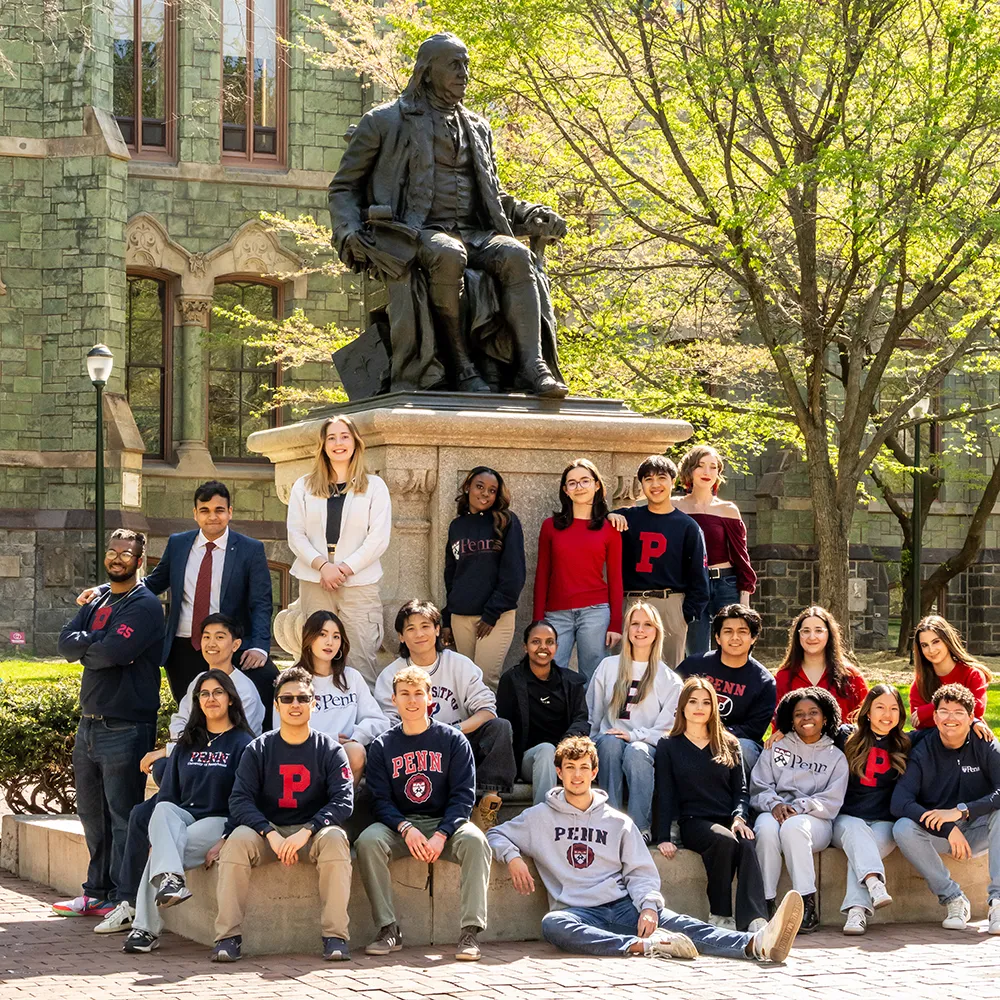 A large group of University of Pennsylvania students gathers at the base of the Ben Franklin statue on campus.