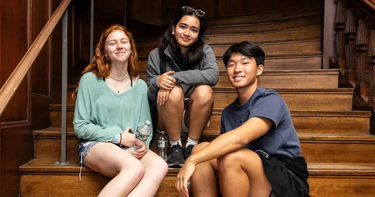 Penn students take a break and chat casually on an elegant wooden staircase, capturing the welcoming environment of student life.