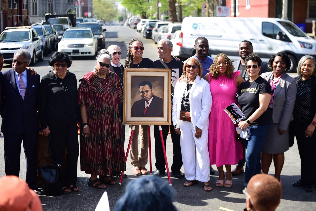 Attendees at the Paul Robeson House and Museum’s 125th anniversary gather around a portrait of Paul Robeson