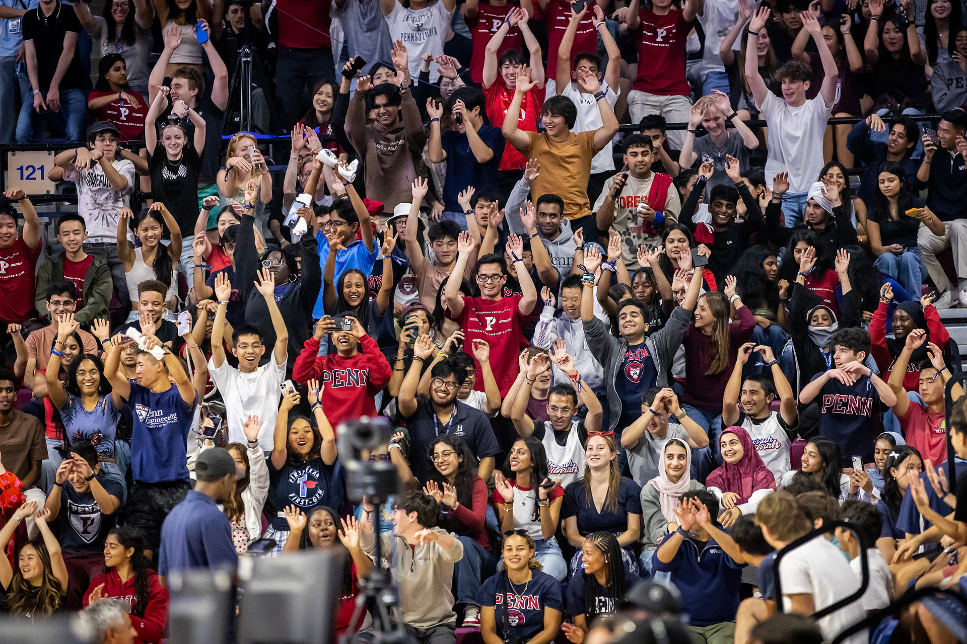 Members of the incoming class of Penn students raise their hands and smile during the “Building the Penn Community” event at the Palestra.