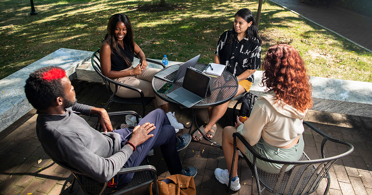 Students in the Social Justice Scholars Program at Penn's School of Social Policy and Practice (SP2) sit around an outdoor table near College Green at the University of Pennsylvania.