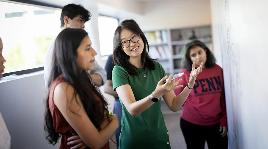 Graduate students gather around a whiteboard, discussing ideas in a classroom setting at the University of Pennsylvania.